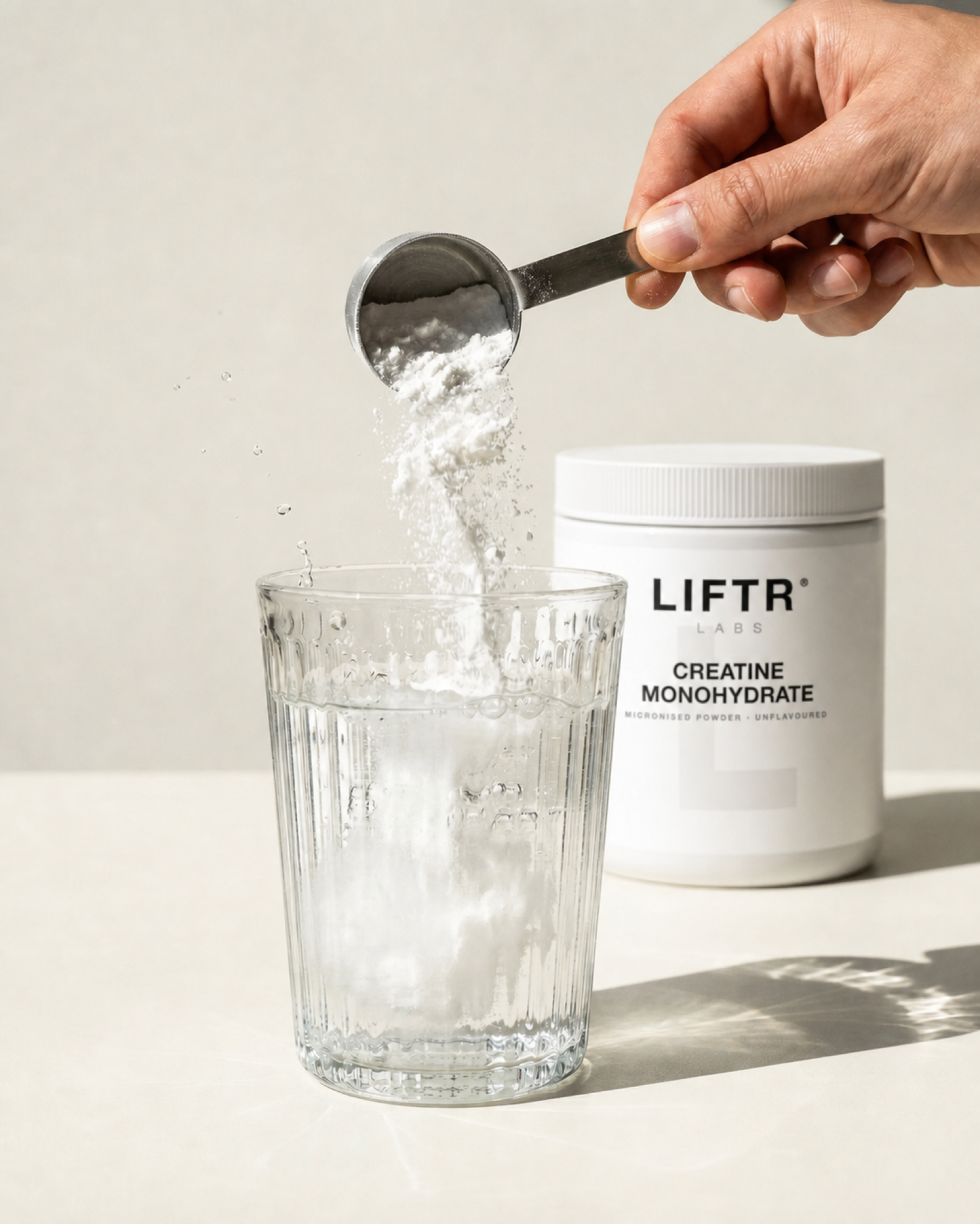Scooping LIFTR LABS creatine monohydrate into a glass of water